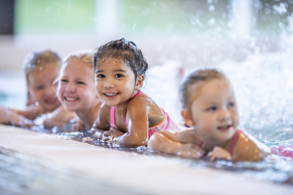 Lachende Kinder am Beckenrand plantschen im Wasser